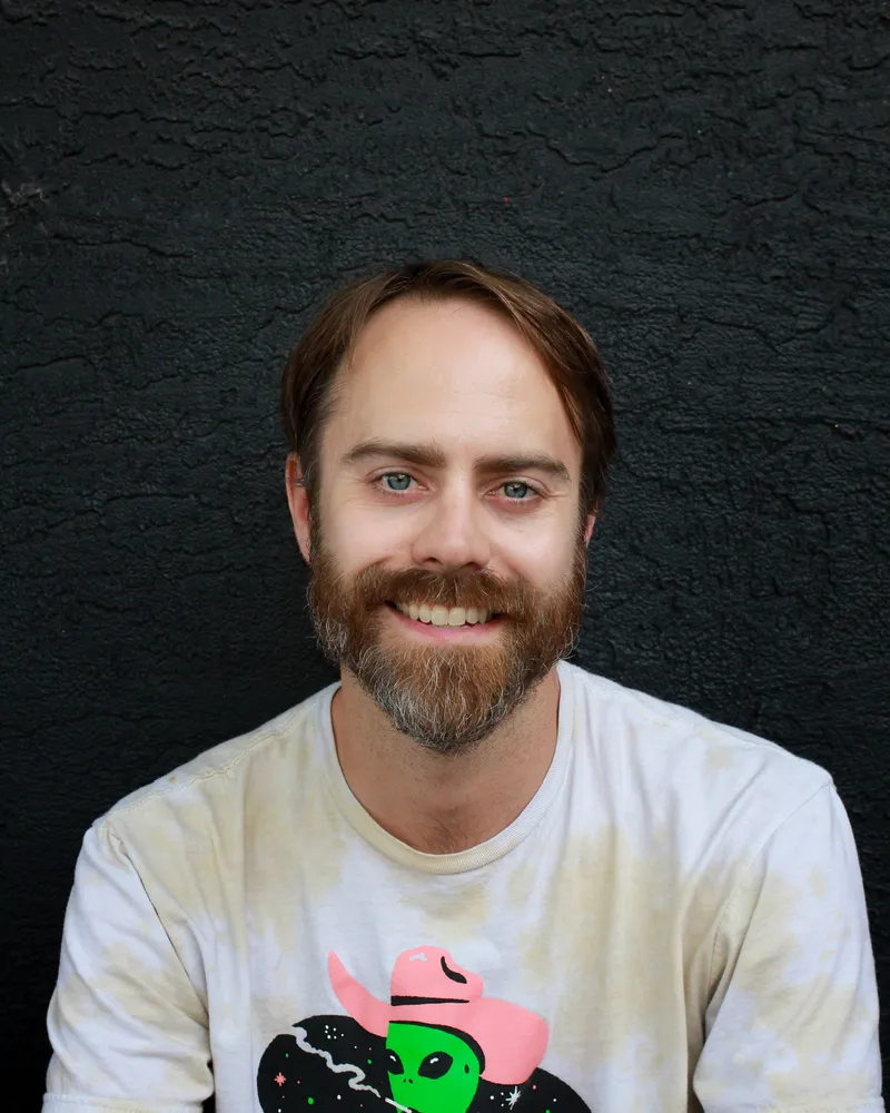 Jordan Clermont smiling, in a graphic T-shirt, against a dark wall