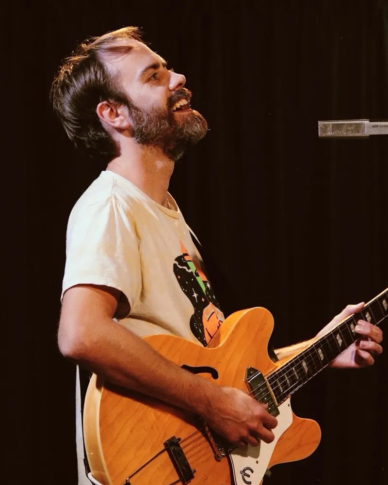 Jordan laughing mid-song, playing an orange Epiphone Casino guitar