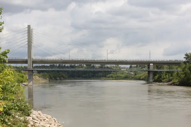 A cable-stayed pedestrian bridge spans a wide river under an overcast sky.