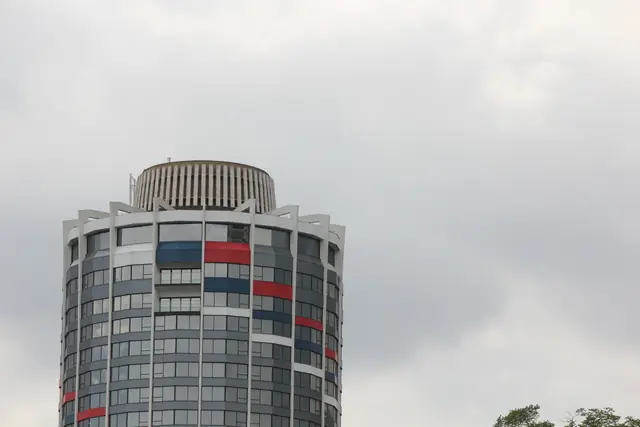 The rounded top of a high-rise with red and blue panels against a cloudy sky.