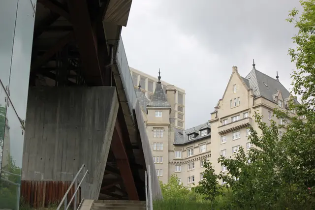 A modern building's angular roofline beside the turreted towers of a historic stone hotel.