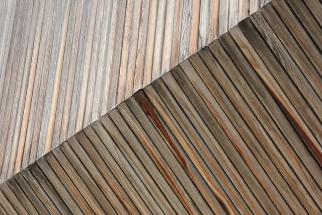 Two sections of weathered wood planking meet at a diagonal seam, grain running in different directions.