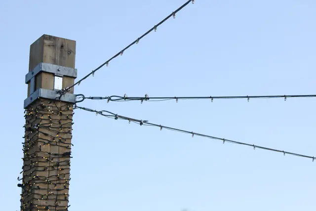A wooden post strung with lights beneath overhead wires against a clear sky.