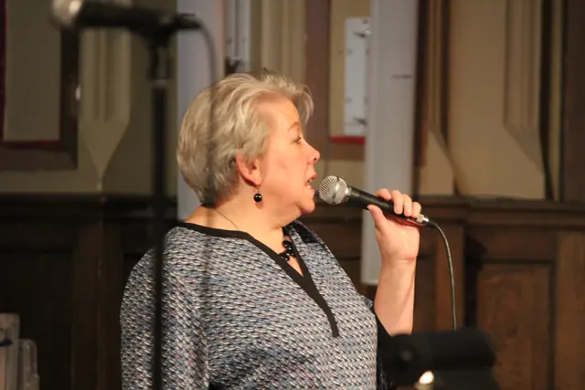 A woman sings into a handheld microphone in profile on a stage.