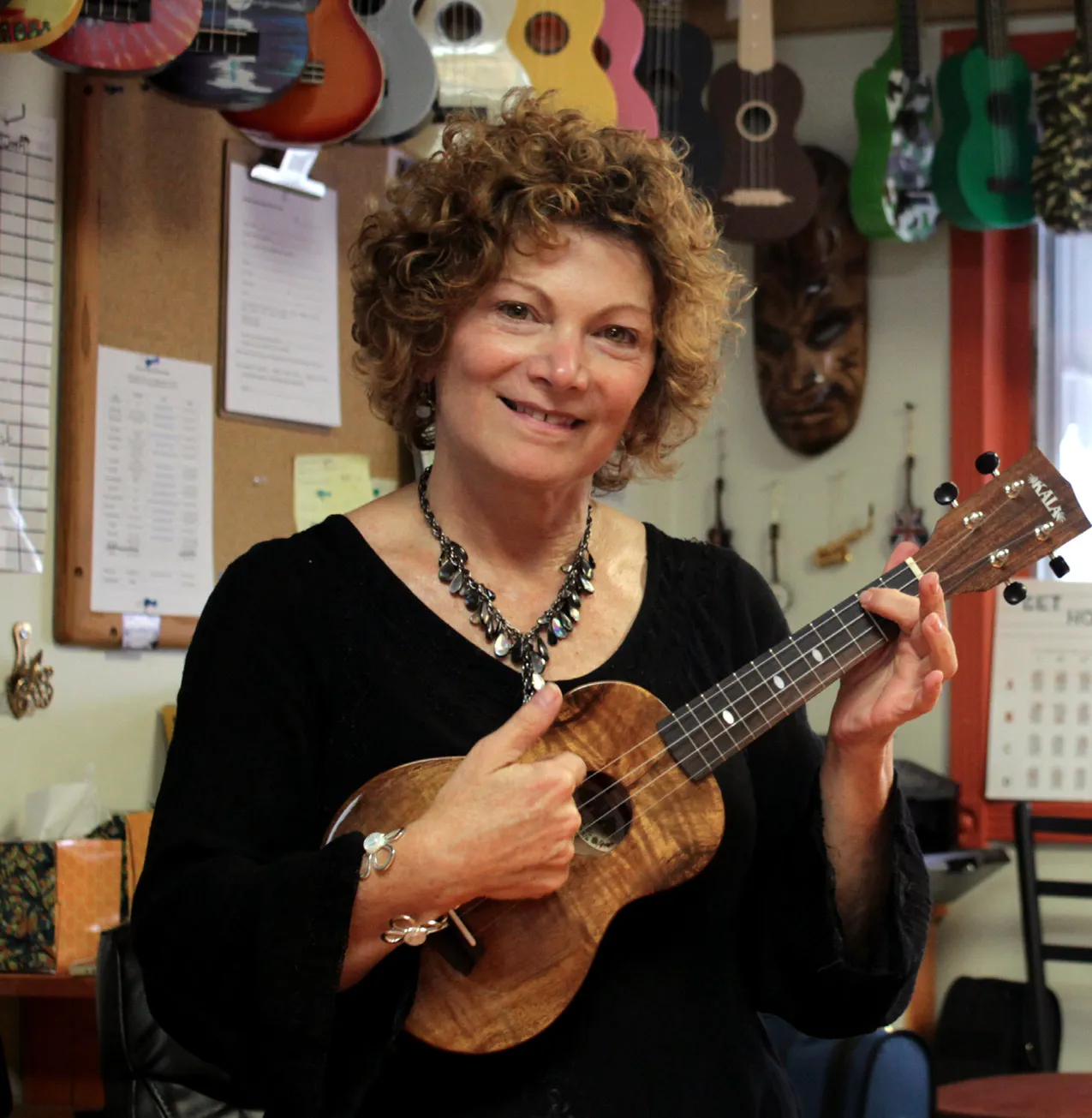 Paula Hirson holding a ukulele inside the Bowtown Music shop, with guitars and ukuleles hanging on the wall behind her.